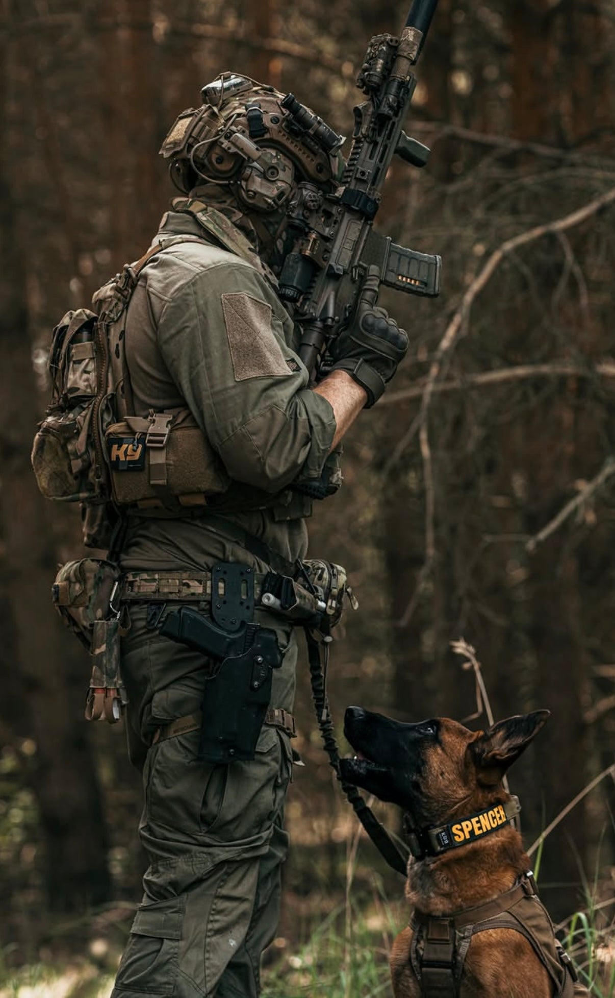 Soldier in tactical gear with a rifle walking a dog in a forest setting