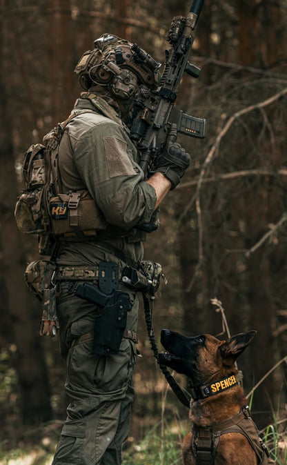 Soldier in tactical gear with a rifle walking a dog in a forest setting